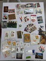 Overhead photo showing the assorted collection of vintage cards, gift tags, and postcards spread across a flat surface, displaying a variety of holiday, floral, and art designs.
