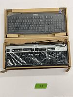 Top-down view of the Dell PS2 keyboard in black, sealed in plastic within a cardboard box showing the full key layout including function keys and numeric keypad.