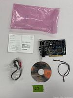Photo of the RME Digi 96/8 PAD PCI audio card with included accessories arranged on a surface: pink anti-static bag, user manual, RCA cable, driver CD, and a small connector cable.