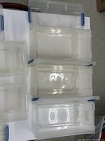 Top open view showing interior space of four clear plastic CD/DVD storage boxes with blue latches, arranged on a white surface.