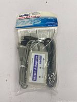 Front view of unopened Gravis MIDI Adaptor in original packaging showing white adaptor and cables.