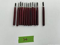 Set of 12 linoleum carving tools with reddish wooden handles and metal blades laid out in a row, one tip loose.