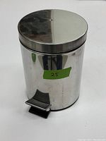 Front and side view of the small round stainless steel step-on trashcan showing the pedal and dented lid.