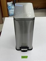 Front view of the rectangular stainless steel waste can showing the pedal and overall condition.