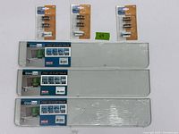 Three rectangular glass shelves stacked with original product labels from Dolle showing the Glassline series. Above the shelves are three unopened packages of three metal shelf supports labeled Flac model from Dolle.