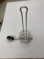 Toilet paper holder displayed vertically with metal wire circular base and tall handle. Tape measure next to holder shows size scale.