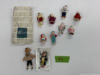 Top view of 10 vintage hand knitted dolls, tree ornament, two other dolls, and fabric pouch with 'Magasin' label.