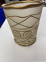 Front view of frosted hammered wastebasket with gold tone swirl and line design and wavy gold rim