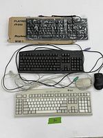Three wired PS/2 keyboards and two wired mice arranged on white background. One keyboard is a white Sun keyboard, one is a black Dell keyboard, and one is a black generic keyboard in plastic on top of its box. Two wired mice included: one white Sun mouse and one black mouse.