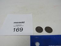 Photo showing two Indian Head pennies side by side next to a ruler for scale and a MaxSold auction number card 169.
