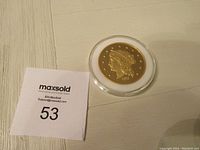 Full view of the 1877 gold coin replica with a MaxSold tag reading "53" to identify the lot.