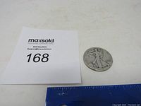 Photo of the 1941 Walking Liberty Silver Half Dollar coin showing front with date and inscriptions visible, alongside a MaxSold card and ruler for scale.