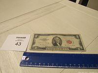 Image of front of 1953 red seal $2 bill showing full bill with ruler for scale and identification tag nearby.