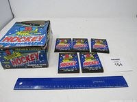 Overview of five unopened packs of 1990 Bowman hockey cards alongside the original box, with a ruler for scale.