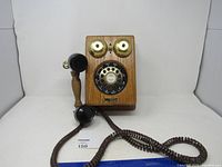 Front angled view of the wooden rotary dial telephone showing handset and cord with brass bells and rotary dial.