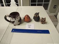 Full lot of four owl figurines and one owl mug displayed on white table with ruler for scale.