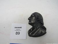 Side profile of small cast metal bust of George Washington with auction label and ruler for scale