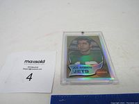 Holographic replica Joe Namath football card in clear plastic protection case on white surface with MaxSold tag.