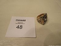 Photo of the ring placed on a flat surface with a MaxSold card showing lot number 48