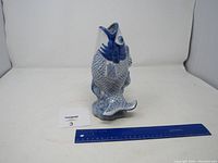 Front and side view of a blue and white porcelain fish figurine shown next to a ruler for size reference.