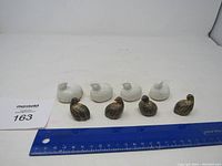 Front view showing all 8 quail figurines arranged in two rows: 4 brown speckled in front, 4 white in back, ruler nearby for scale.
