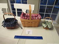 Three Longaberger baskets with different colored liners placed on a white table with ruler for scale.