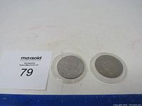 Two Eisenhower dollar coins in protective cases, one dated 1972 and the other 1974, shown side-by-side with a ruler for scale.