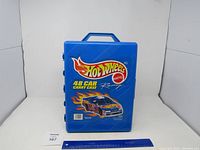 Blue Hot Wheels branded plastic carry case with handle for 48 cars placed in front of plain white background with measuring ruler.