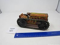 Side view of vintage Marx windup tin tractor showing colorful painted tin construction, rubber treads and windup key mechanism next to a measuring ruler for scale.