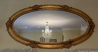 Full view of large oval mirror reflecting chandelier and room.