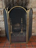 Front view of trifold brass fireplace screen showing central arched panel and side panels with mesh inserts