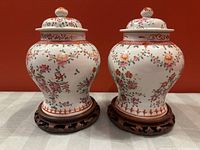 Front view of both ginger jars with lids on stands against a red background