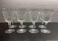 Front view of eight glasses in two rows on black surface against white tile background