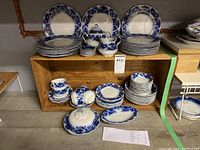 Overall display of dishes on wooden shelves including plates, cups, sugar bowl and creamer
