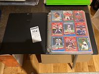 Black binder open displaying a page of baseball cards in plastic sleeves, showing 9 cards per page in mostly 1980s and 1990s style.
