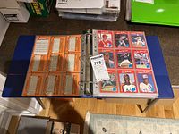 Open binder on table showing multiple baseball cards from the 1980s and 1990s in plastic sleeves, front and back of cards visible.