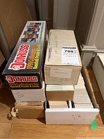 Six cardboard boxes of baseball cards including unopened 1990 set and 1991 Donruss Collector's Set visible on floor.