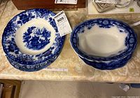 Wide view of blue and white flow blue dishes, including a deeply set bowl with floral and scenic design, and oval serving bowl