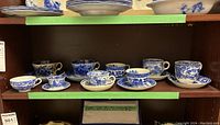 Shelf with eight sets of blue and white tea cups and saucers, varying sizes and intricate designs, visible crazing and signs of age.