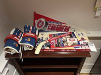 Photo showing blue, red, and white Cooper branded leather hockey gloves, a white mini hockey stick with a red band reading 'Montreal Canadiens,' and a red and white Montreal Canadiens pennant with logo.