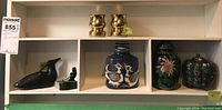 Shelf with Inuit carved jade fishing figure, carved loon figurine, Royal Copenhagen bird vase, cloisonné chrysanthemum jar, and cloisonné pumpkin-shaped vase.