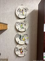 Four collector plates hung vertically on a wall, showing entire set with plate hanger attached.