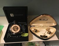 Mechanical movement pocket watch in black presentation box, showing dial and chain inside box interior.