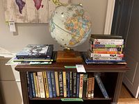 Full view of the globe on a wooden stand surrounded by stacks of books about travel and baseball on a wooden table.