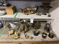 Shelf with assortment of metal and ceramic items including a large metal pitcher, ceramic salt and pepper shakers, two-tiered metal stand, and silver-plated creamer and sugar bowl.