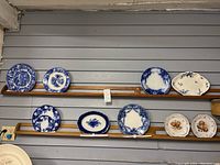 Shelf display of 10 plates and platters with various blue and white flow blue patterns and bird illustrations.