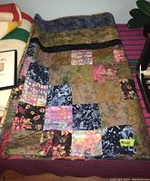Full view of patchwork quilt folded on a surface, showing multiple patterned squares and color variety.
