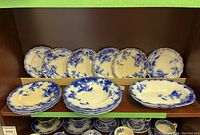 Set of approximately 14 antique Ridgway blue and white dishes with scalloped edges, displayed on wooden shelves