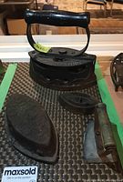 Top-down view of three cast iron sad irons including the large SELF HEATING iron, child's sad iron, and another smaller iron with wooden handle.