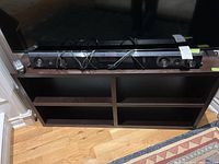 Full view of Samsung sound bar with remote placed on a wooden stand below a television.